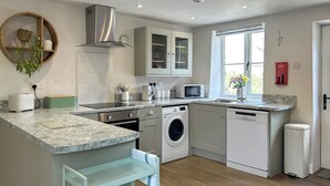 A modern kitchen with a built-in washing machine, a microwave, and a sink. - Mawstone Mine Cottage (Youlgrave)