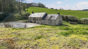 A stone cottage with a sloped roof, a small porch, and a wheelbarrow outside. - Mawstone Mine Cottage (Youlgrave)