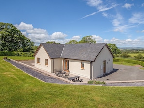 A single-story house with a sloped roof, a front porch with a table and chairs, and a driveway leading to the entrance. - 4 bedroom accommodation in Narberth (Narberth)