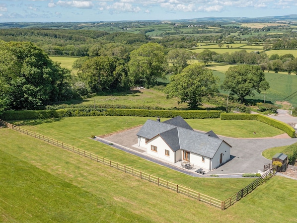 A house with a paved driveway, surrounded by a fenced lawn, set in a rural landscape with rolling hills and trees in the background. - 4 bedroom accommodation in Narberth (Narberth)
