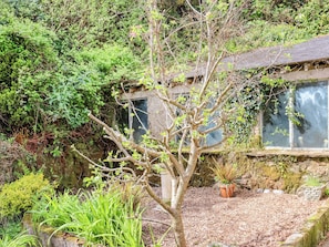 A rustic stone building with a garden in front, surrounded by dense greenery. - Wren Cottage Apartment (Fishguard)