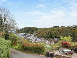A hillside view of a town with a road leading down, a bench, and a table with chairs.
