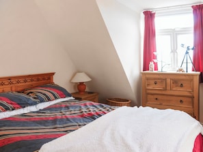 A bedroom with a bed, a nightstand, a lamp, a dresser, and a window with curtains. - Wren Cottage Apartment (Fishguard)