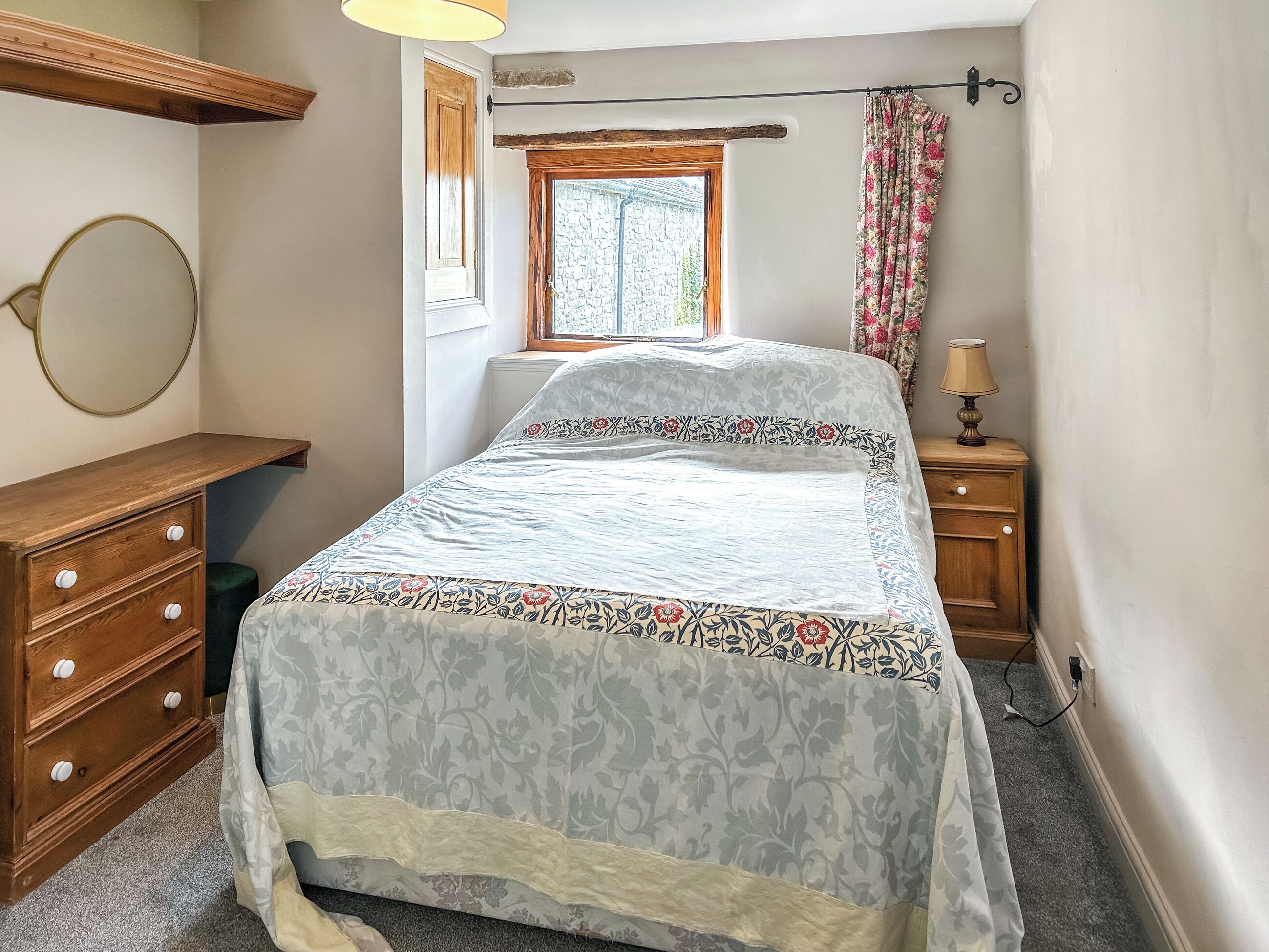 Une chambre à coucher comprenant un lit, une commode, une table de chevet, une lampe, une fenêtre et un miroir.