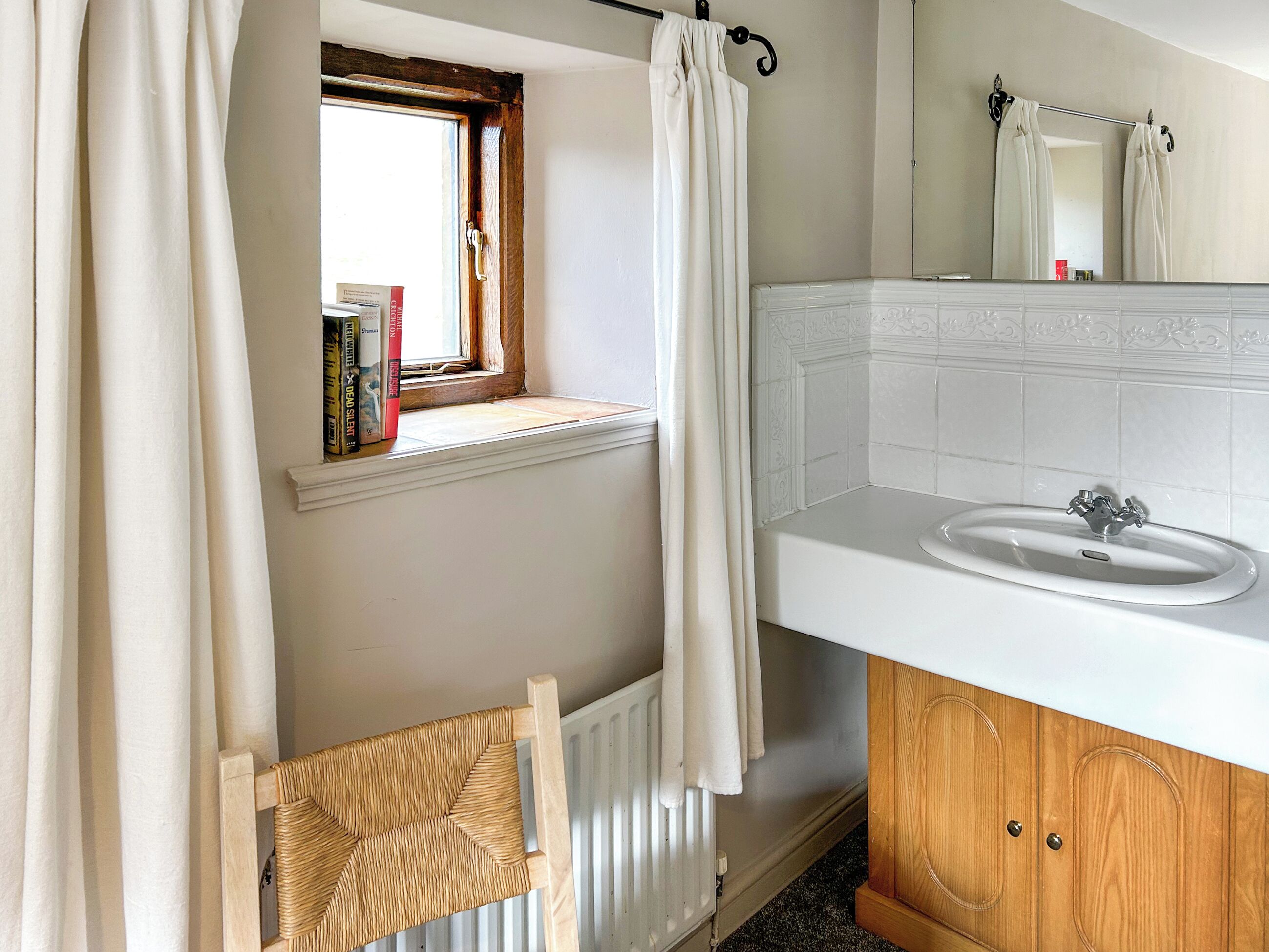 A bathroom with a window, a white sink, wooden cabinets, and a radiator.