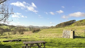 Et picnicbord i en græsplæne med en stenvæg og et metalhegn.