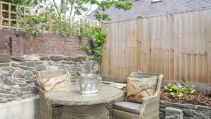 Ein Gartenmöbel-Set aus Rattan mit Stühlen, ein Metall-Eimer und eine Steinmauer.