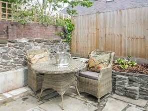 A wicker patio table with chairs, a metal bucket, and a stone wall. - 1 bedroom accommodation in Conwy (Conwy)