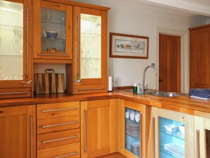 Eine Küche mit Holzausstattung, einer Vitrine mit Glastüren, einem Spülbecken und einem gerahmten Bild an der Wand.