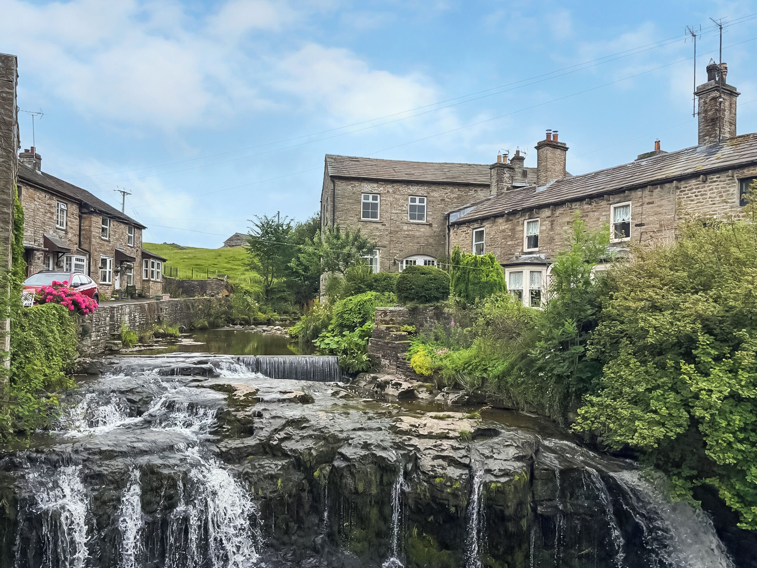 Un bâtiment en pierre avec une cascade, entouré de verdure et sous un ciel dégagé.