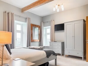Ein Schlafzimmer mit Bett, Nachttisch, Lampe, Kleiderschrank und Fernseher.