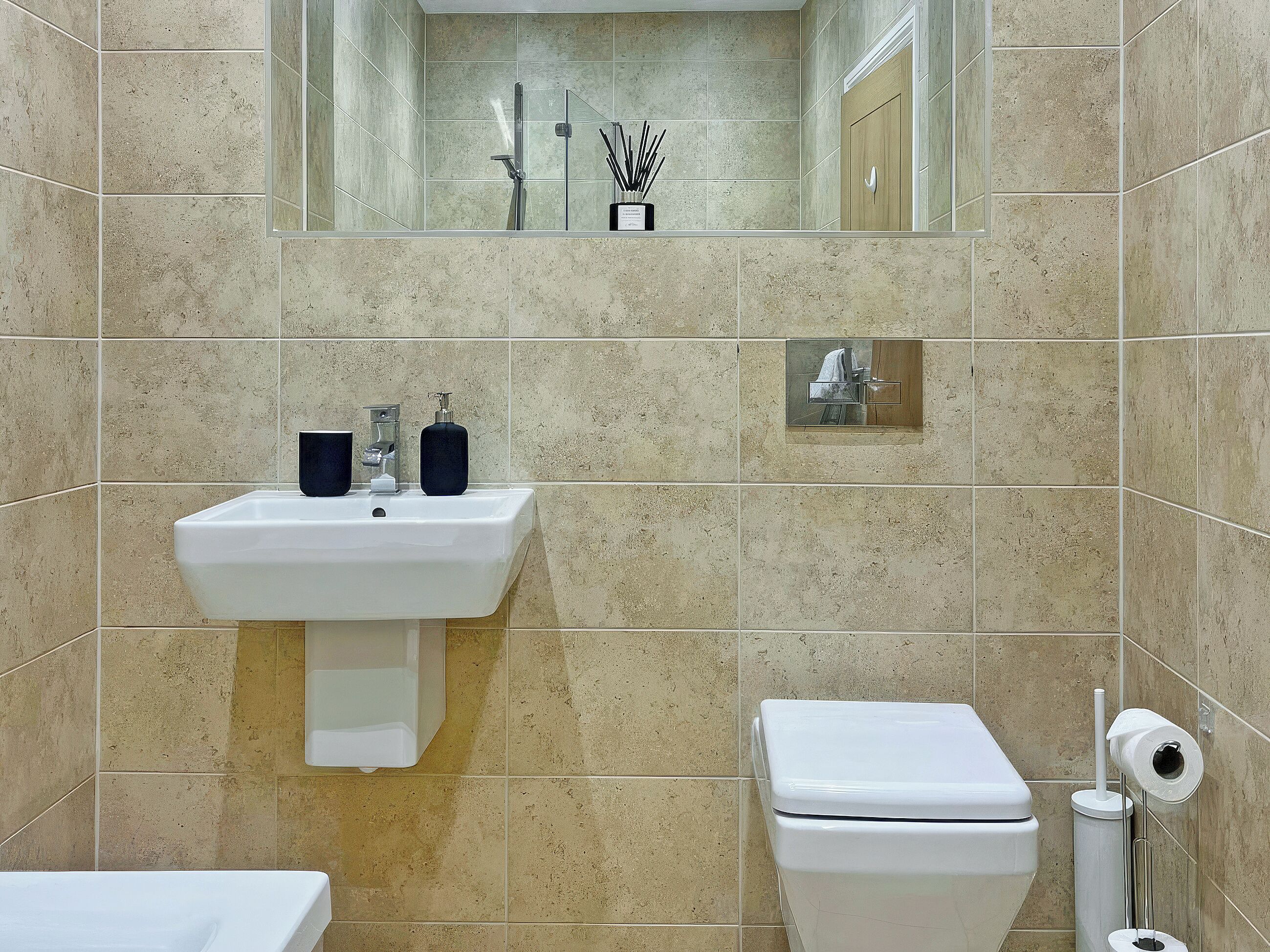 Een badkamer met een wastafel, spiegel, toilet en een klein spiegeltje boven het toilet.