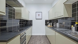 Een moderne keuken met zwarte aanrechtbladen, roestvrijstalen apparatuur en een betegelde spatwand.