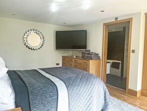 Un dormitorio con cama, televisión, cómoda de madera y puerta al baño.