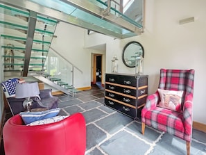 Un interior moderno con una escalera, un sillón de cuero rojo, un sillón de cuadros y un mueble de almacenaje negro.