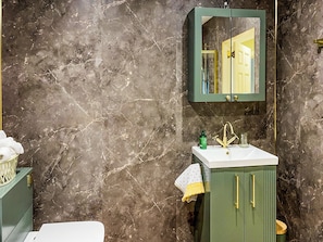 A bathroom with a marble wall, a green cabinet with gold handles, a white sink, and a mirror above the cabinet. - 1 bedroom accommodation in Strathtay (Strathtay)