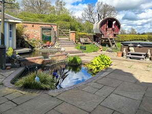 Ein Garten mit Teich, einer Holzbank, einer Statue und einem rot gestrichenen Fachwerkhäuschen.
