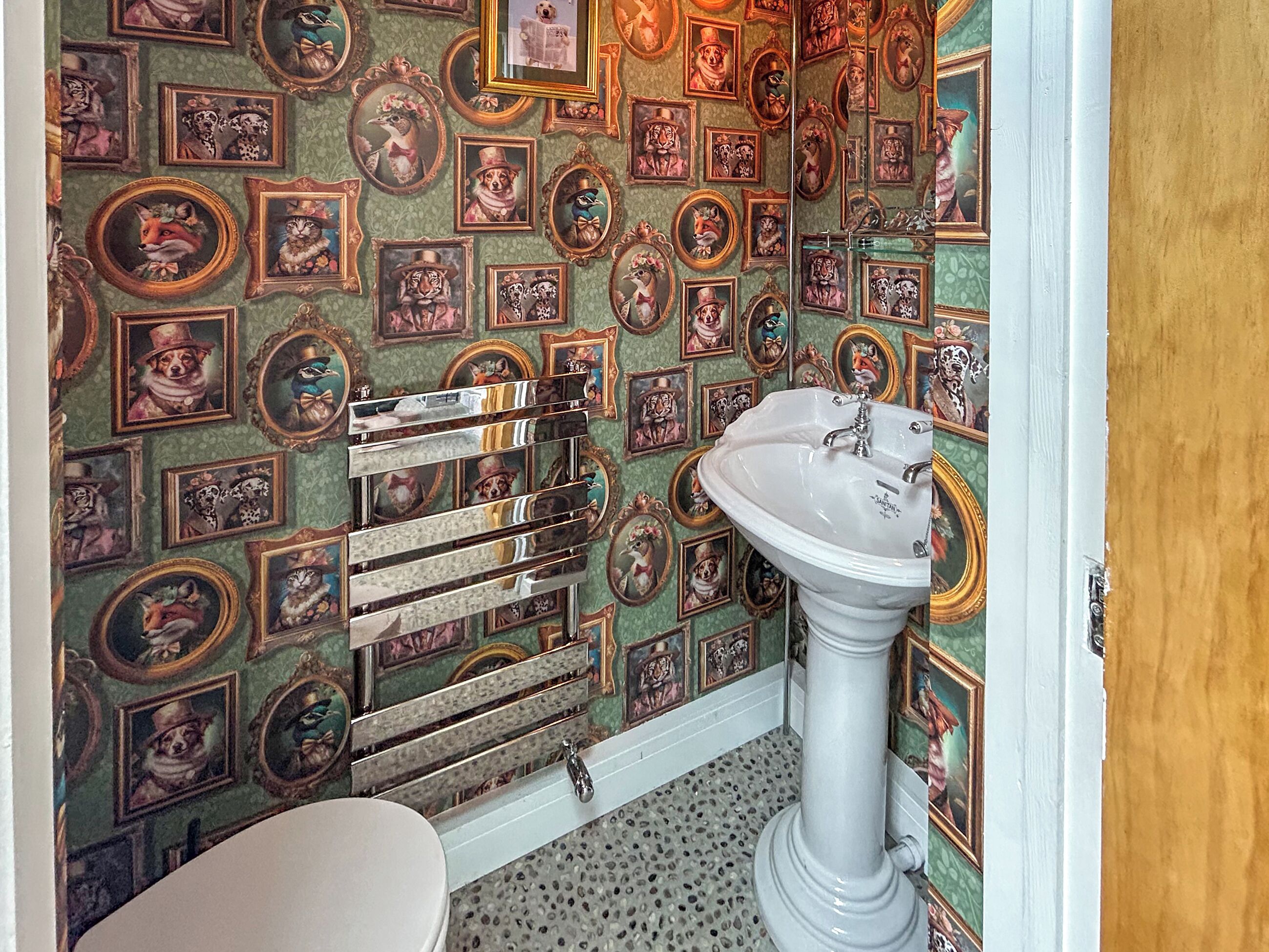 A bathroom with a patterned wallpaper, a white pedestal sink, and a towel rack.
