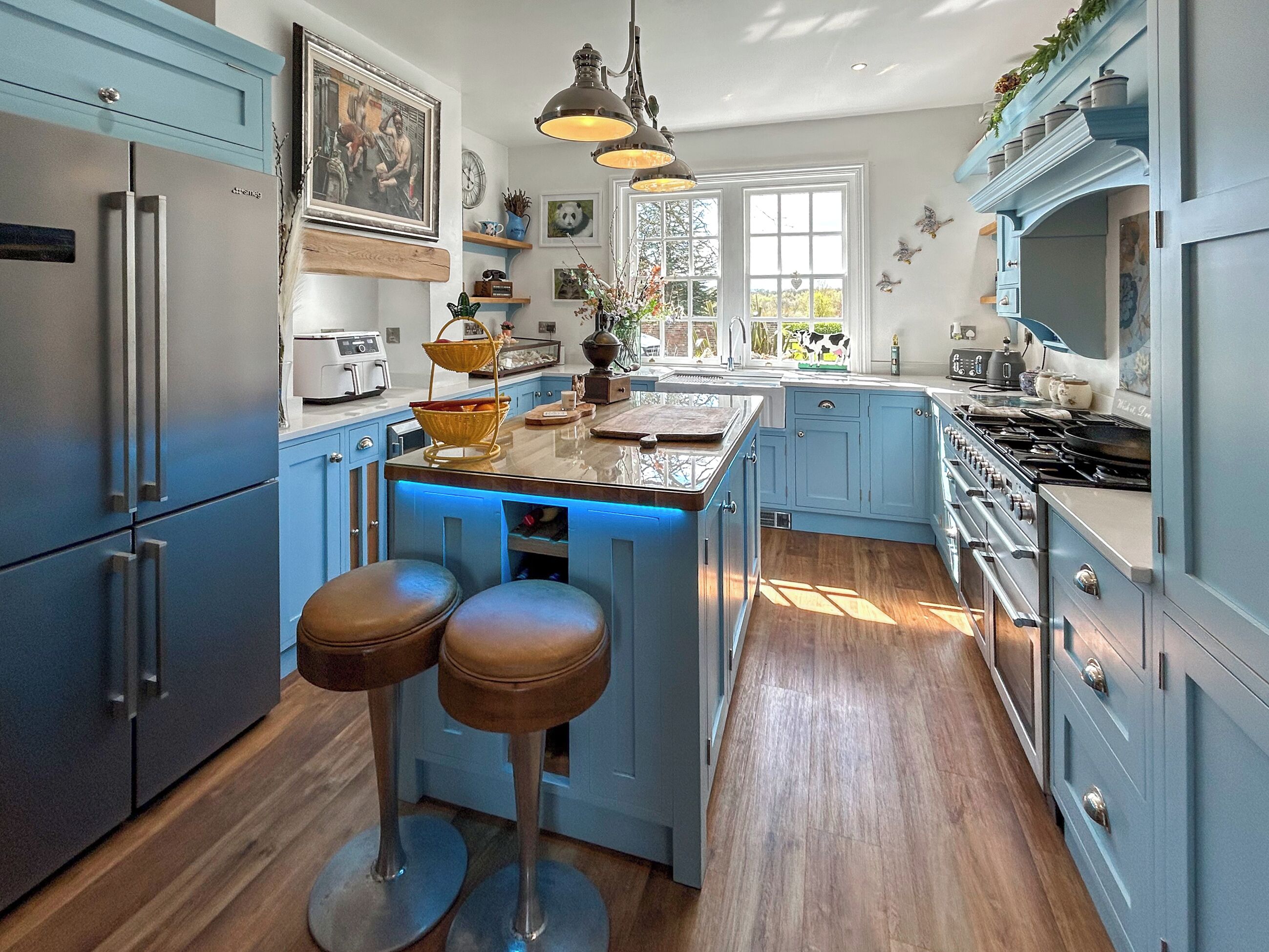 Une cuisine avec des meubles bleus, un îlot central doté de tabourets, une cuisinière et divers appareils de cuisine.