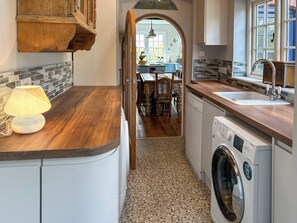 Eine Küche mit einer Holzausziehtheke, einer Waschmaschine und einem Essbereich, der durch einen Bogen sichtbar ist.