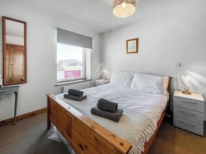 Une chambre avec un lit en bois, une fenêtre donnant sur un beau paysage, une table de chevet avec une lampe et un luminaire fixé au mur.