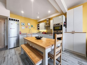 Cocina compacta con una mesa de madera, banco, electrodomésticos de acero inoxidable y una pared amarilla.