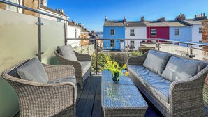 Ein Balkon mit Korbmöbeln, einem Glastisch und einem Blumenvasen.