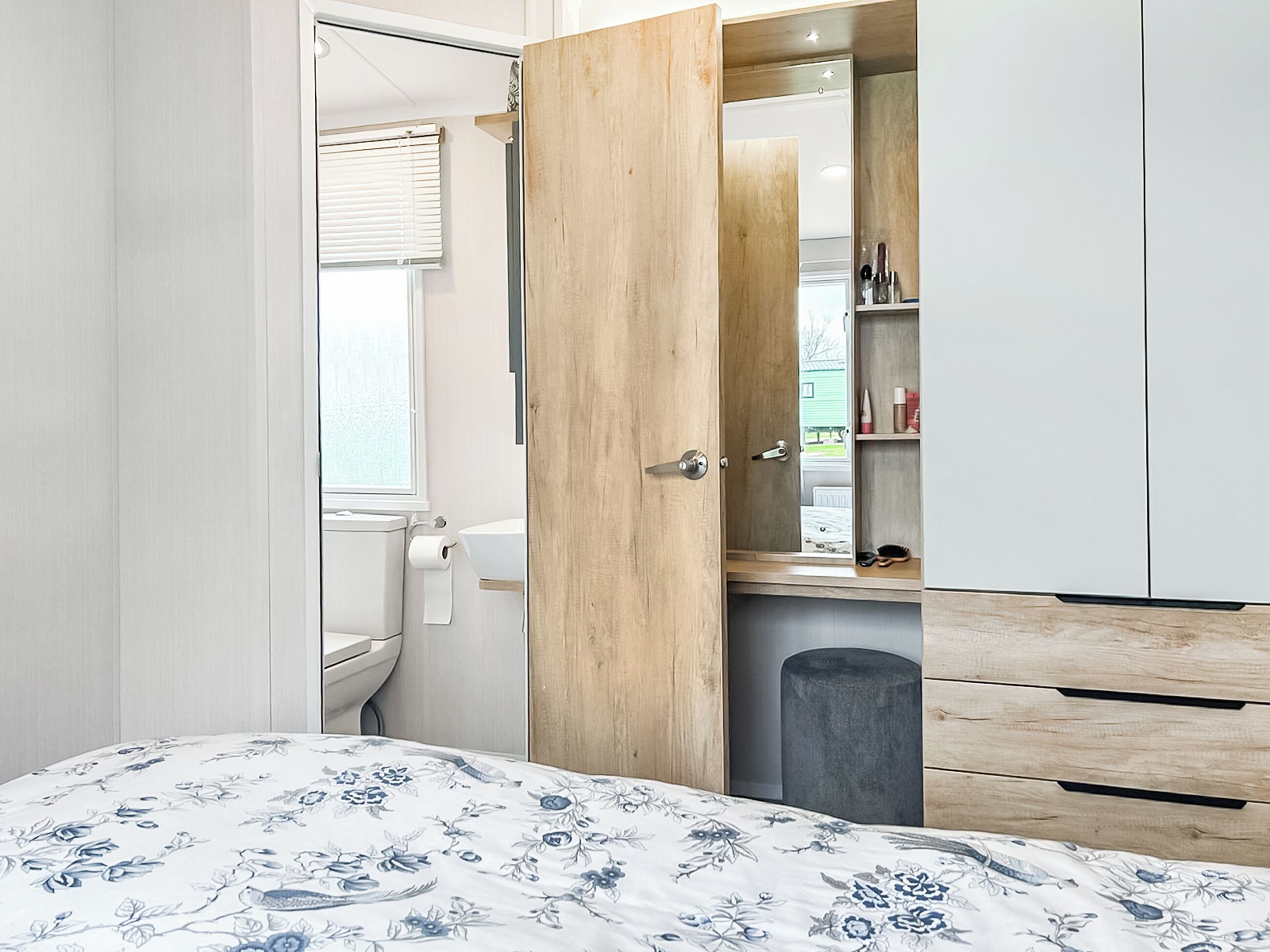 Quarto com cama, guarda-roupa de madeira, espelho e janela com persianas.