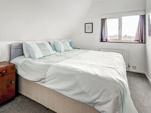 Une chambre à coucher avec un lit, une table de chevet, une fenêtre avec des rideaux et un radiateur.