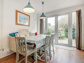 Un coin repas avec une table et des chaises, un banc, un tableau accroché au mur et une vue à travers la porte vitrée.