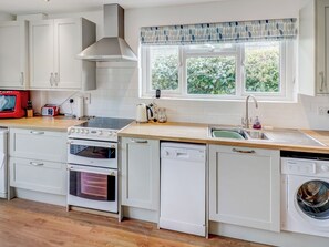 A modern kitchen with white cabinetry, a built-in oven, a dishwasher, a washing machine, and a window with a view of greenery. - Bembridge Coastal Escape (Bembridge)