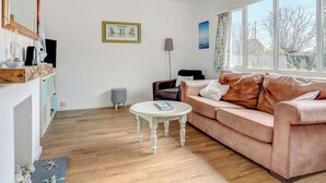 A living room with a wooden floor, a white round table, a brown sofa, a framed picture on the wall, and a window with a view. - Bembridge Coastal Escape (Bembridge)