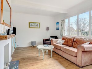 A living room with a wooden floor, a white round table, a brown sofa, a framed picture on the wall, and a window with a view. - Bembridge Coastal Escape (Bembridge)