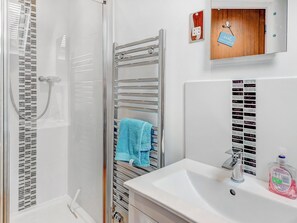 Une salle de bain avec une douche, un porte-serviettes avec une serviette bleue, un lavabo avec un distributeur de savon et une porte en bois avec une pancarte.
