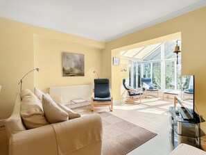 Ein Wohnzimmer mit einer Couch, Sesseln, einer Heizung, einem Bild und einer Glastür, die nach draußen führt.