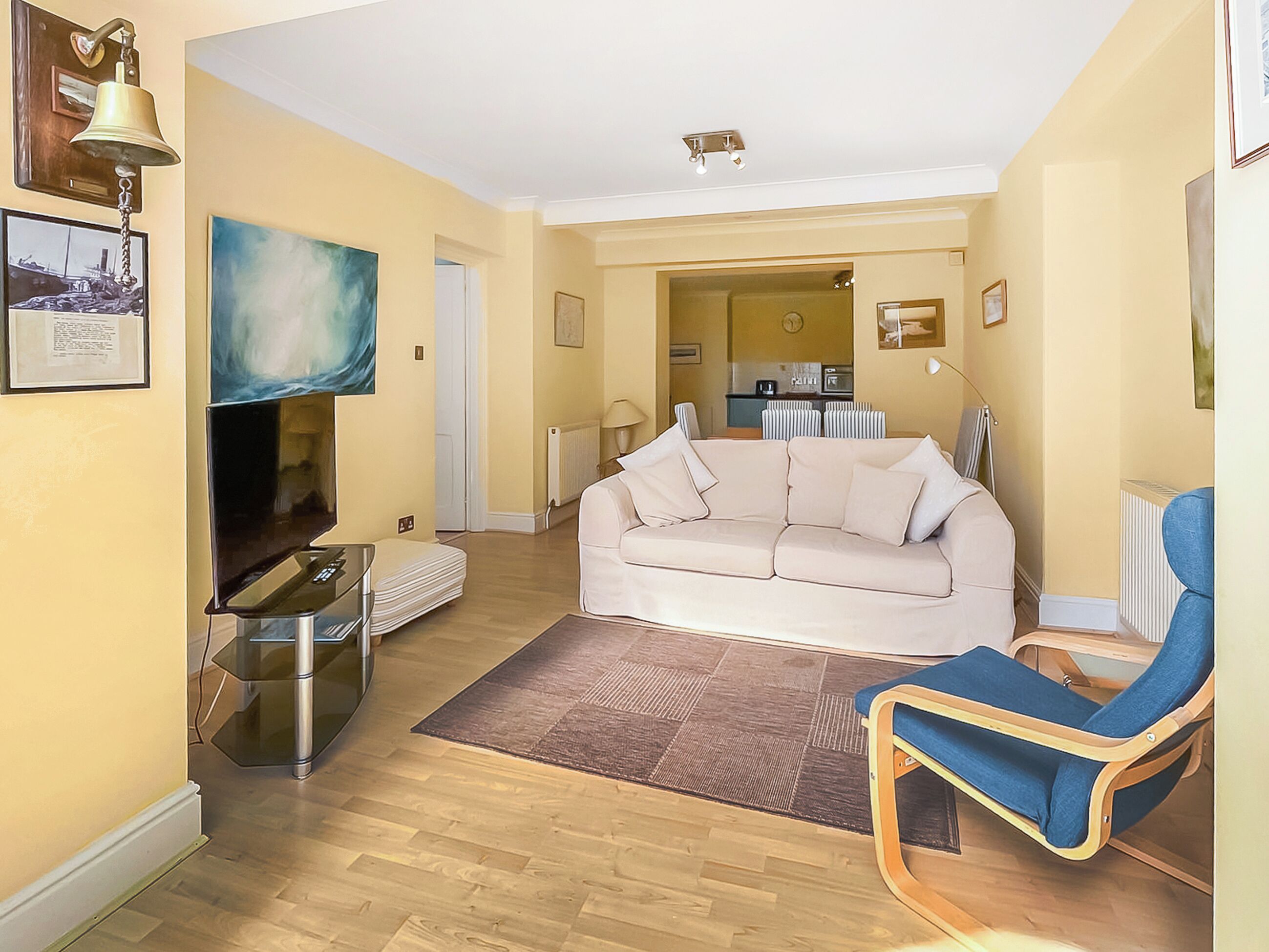 A living room with a sofa, a television, a blue chair, and a dining area in the background.