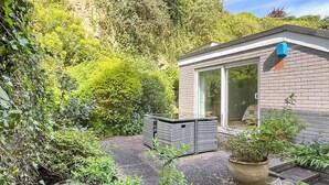 Een modern huis met een terras, een kleine tuin en een raam met uitzicht op de omliggende begroeiing.