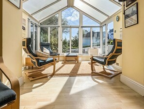 A conservatory with a glass ceiling, wooden flooring, and two lounge chairs with cushions. - 2 bedroom accommodation in Salcombe (Salcombe)