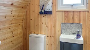 Un baño con paneles de madera, un inodoro blanco, un lavabo con espejo y una ventana sobre el lavabo.