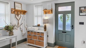 A clean, well-lit entryway with a door, a bench with baskets, a wall-mounted coat rack, and a hanging heart-shaped decoration. - Old Master's Cottage (Leven)