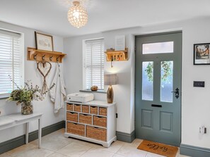 A clean, well-lit entryway with a door, a bench with baskets, a wall-mounted coat rack, and a hanging heart-shaped decoration. - Old Master's Cottage (Leven)