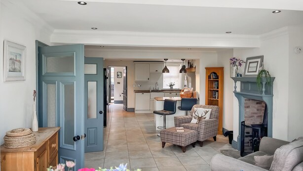 A living room with a sofa, a chair, a fireplace, and a kitchen in the background. - Old Master's Cottage (Leven)