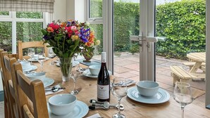 A dining table set with plates, glasses, cutlery, a bottle of wine, and a vase of flowers. - Old Master's Cottage (Leven)