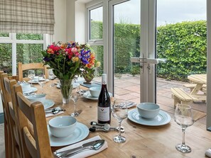 A dining table set with plates, glasses, cutlery, a bottle of wine, and a vase of flowers. - Old Master's Cottage (Leven)