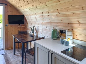 Eine Küche mit Holzwänden, einem an der Wand befestigten Fernseher, einem Tisch mit Stühlen, einem Wasserkocher, einer Tasse und einer Kaffeemaschine.