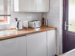 Eine Küche mit weißen Schränken, einem Toaster, einem Wasserkocher und einem Fenster mit Jalousien.