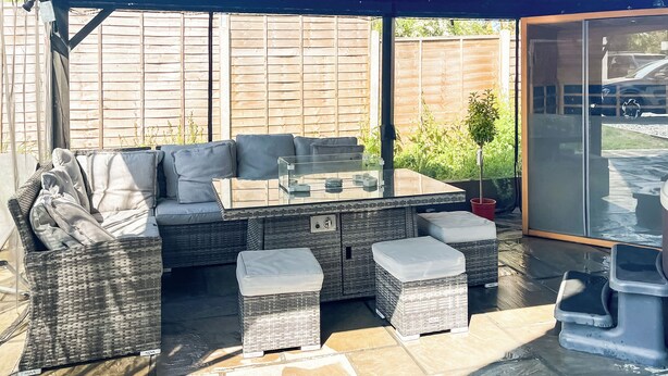Eine Terrasse im Freien mit einer Couch, Hocker und einem Glastisch.