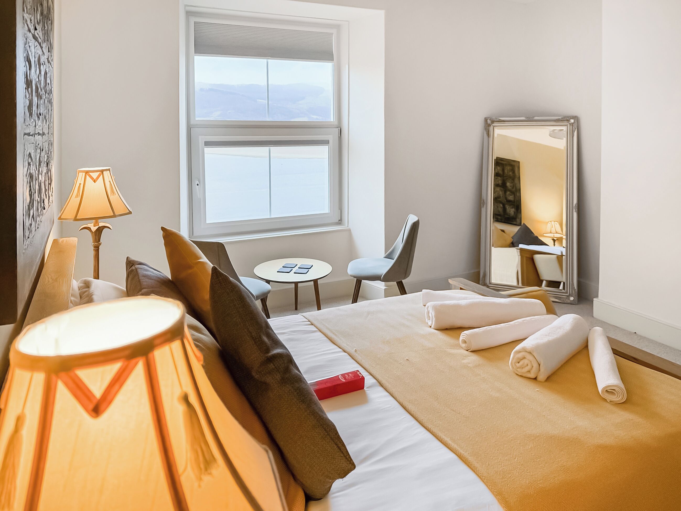 A hotel room with a bed, a desk, a chair, a window, and a mirror.