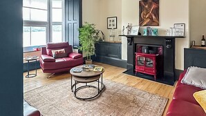 A living room with a red sofa, a coffee table, a fireplace, and a large window.