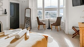 A hotel room with a bed, two chairs, a small table, a mirror, and a view of the outdoors.